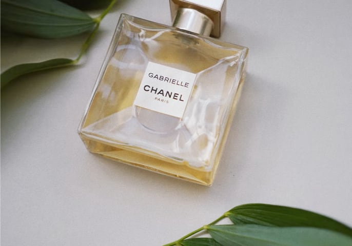 A bottle of perfume laid sideways near green foliage